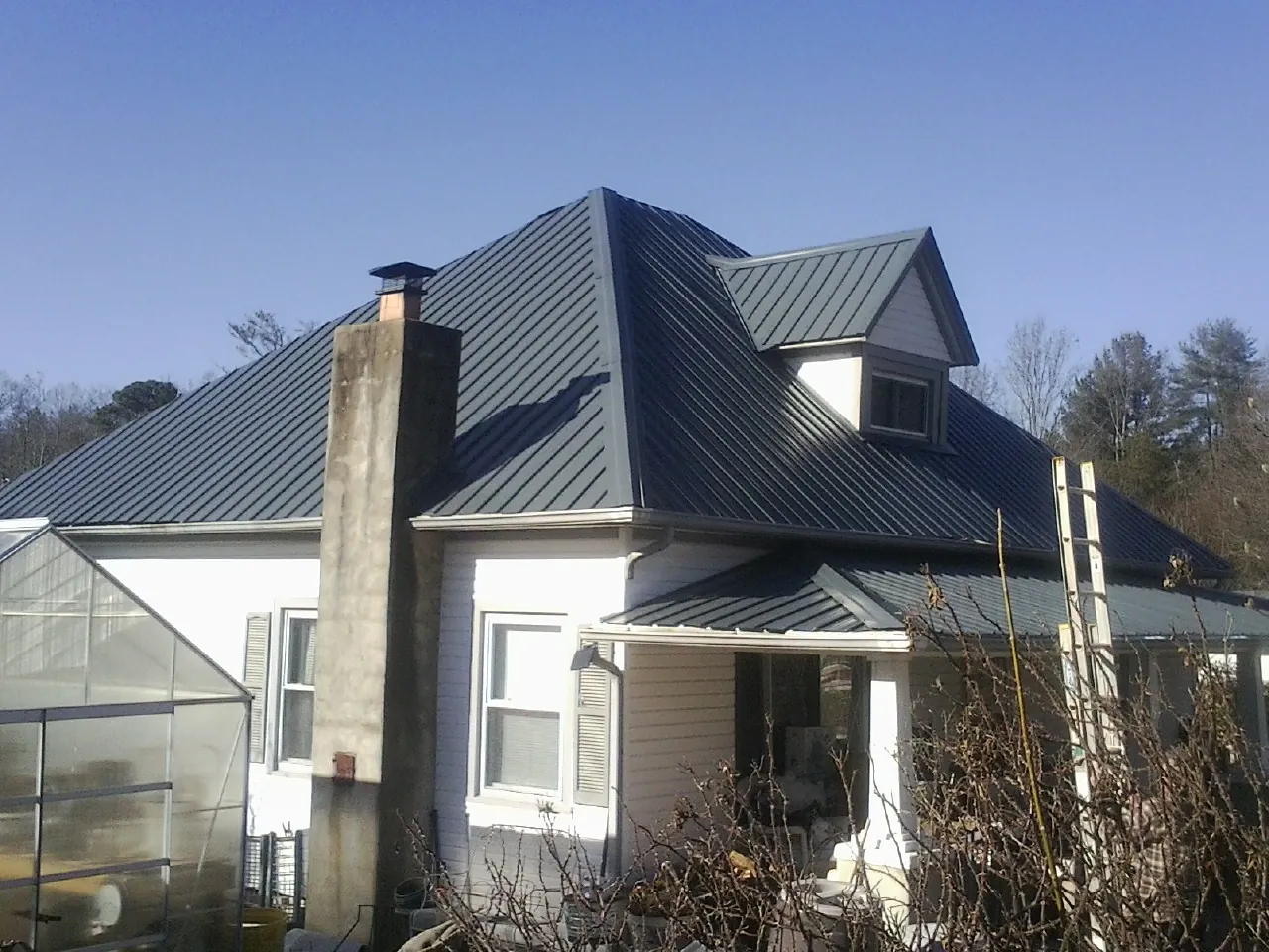 Dark blue standing seam metal roof on a white farmhouse with dormer — Slate & Tile Roof Repair by Roofing Brothers in Prairieburg