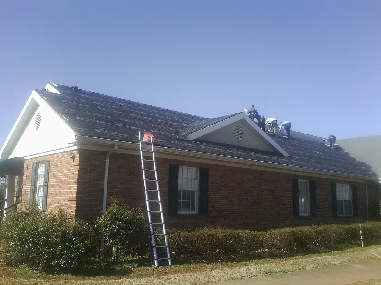 Crew tearing shingles off a brick ranch roof with a ladder set — Metal Roof Repair work by our crew in Prairieburg