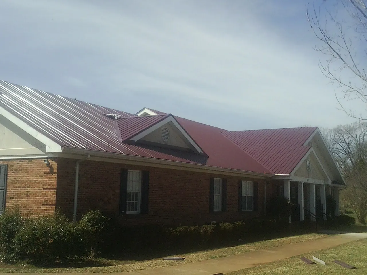 Red metal roof with gabled entries on a long brick building, from a Hail Damage Roof Repair job in Prairieburg