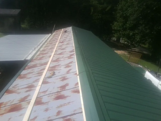 Old rusted panels beside newly installed green metal roofing — Wind Damage Roof Repair by Roofing Brothers in Prairieburg