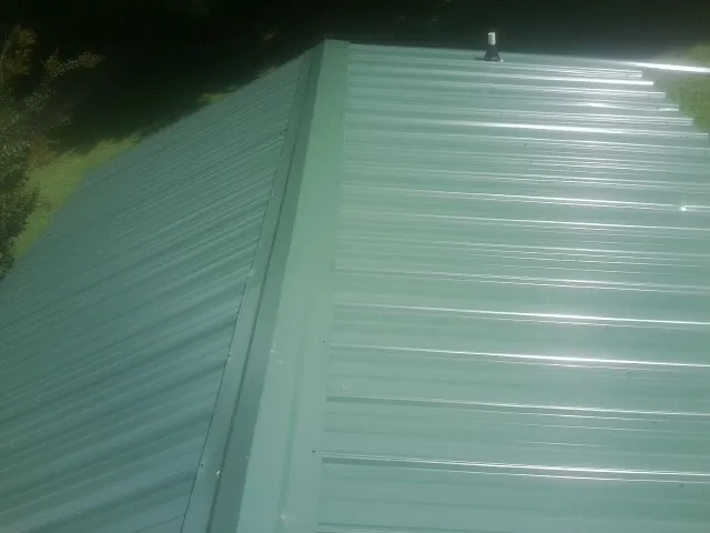 New green metal panels meeting at the ridge of a roof — Flat Roof Repair work by our crew in Prairieburg