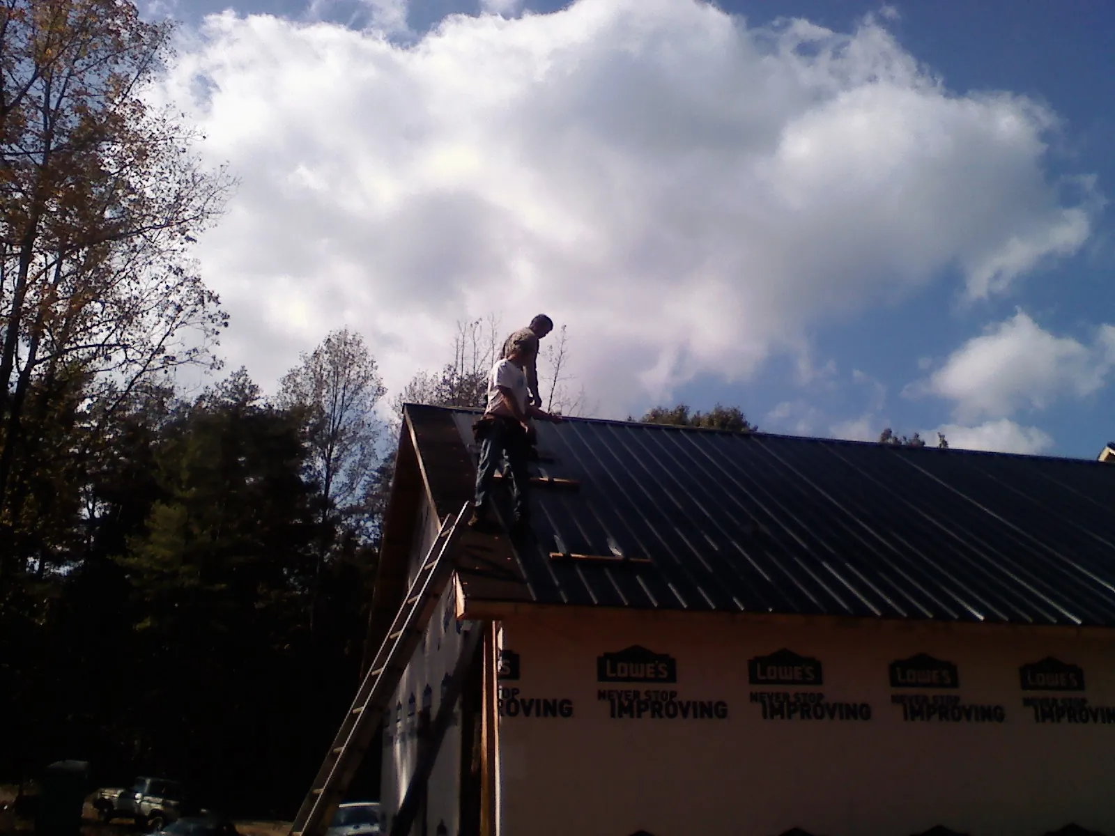 Roofer fastening dark metal panels high against a cloudy sky, from a Roof Inspection job in Prairieburg