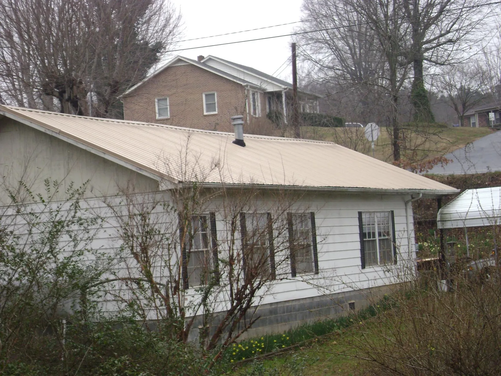 Tan metal roof on a white sided house set into a hillside — Commercial Roofing by Roofing Brothers in Prairieburg