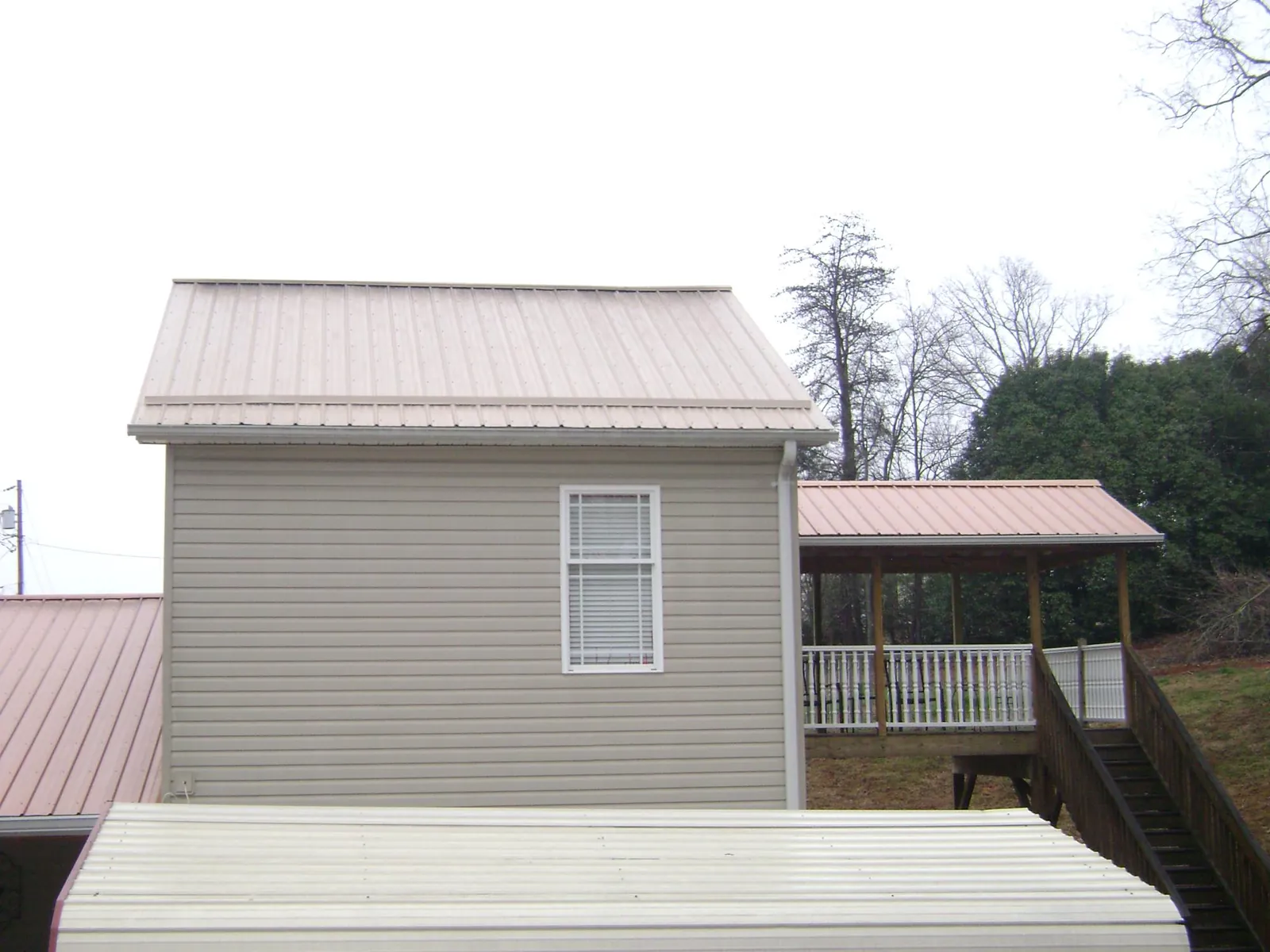 Tan metal roofs on a two story addition and attached porch, from a Roof Replacement job in Prairieburg